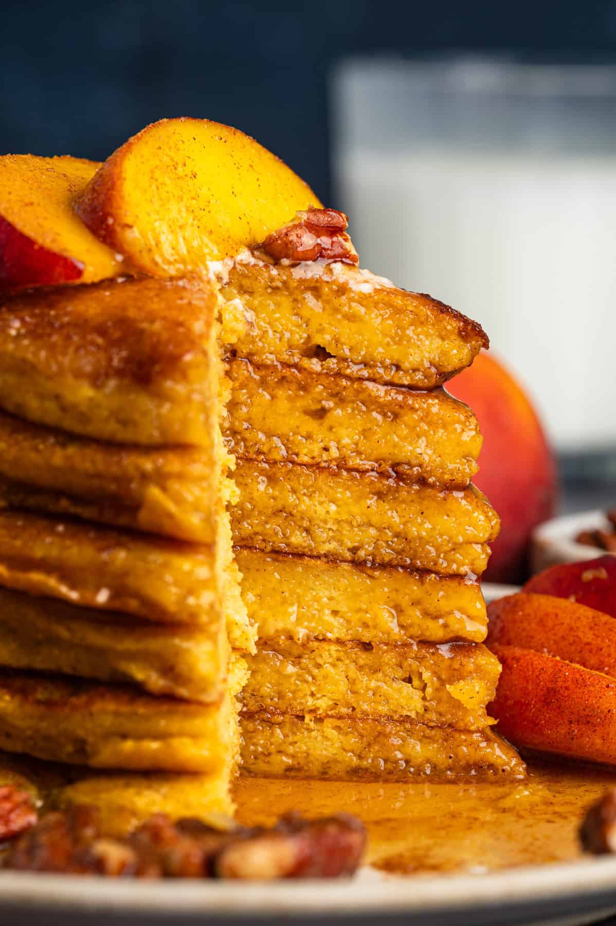 Peach Pancakes with Cinnamon Maple Syrup and Pecans Stack of pancakes with a slice cut out, cake-style, topped with peaches and syrup - on a plate.