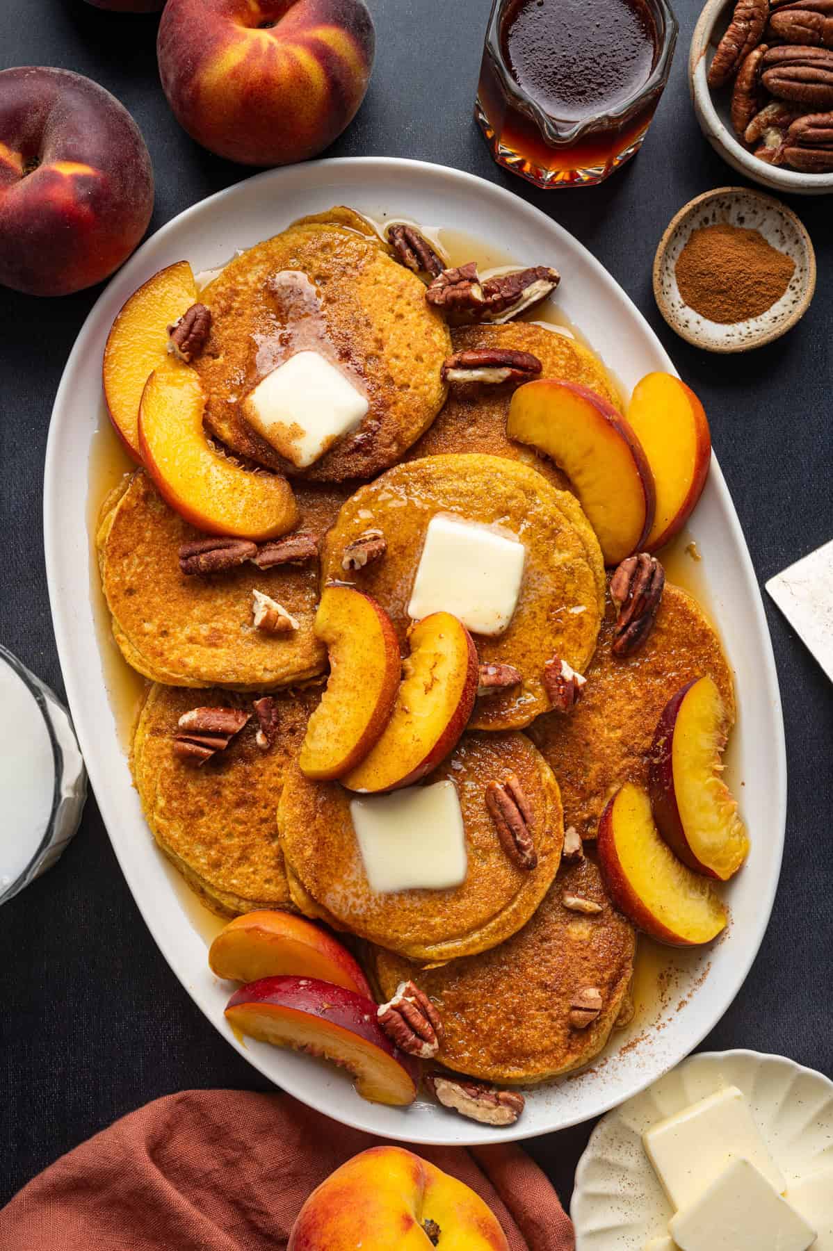 Peach Pancakes with Cinnamon Maple Syrup and Pecans Peach Pancakes with Cinnamon Maple Syrup, Peach Slices, Butter, and Pecans - on a large white platter.