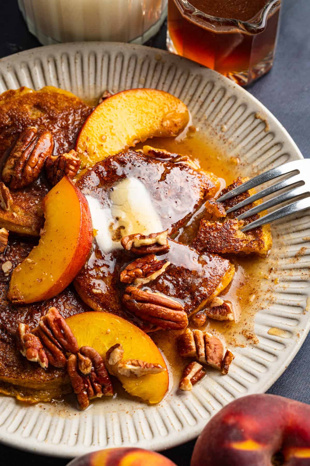 Peach Pancakes with Cinnamon Maple Syrup and Pecans Peach Pancakes with Cinnamon Maple Syrup, Peach Slices, Butter, and Pecans - on a white plate.