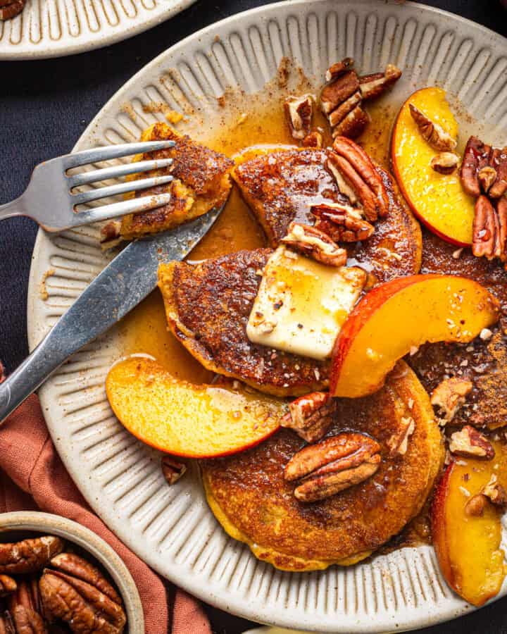 Peach Pancakes with Cinnamon Maple Syrup, Peach Slices, Butter, and Pecans - on a white plate.