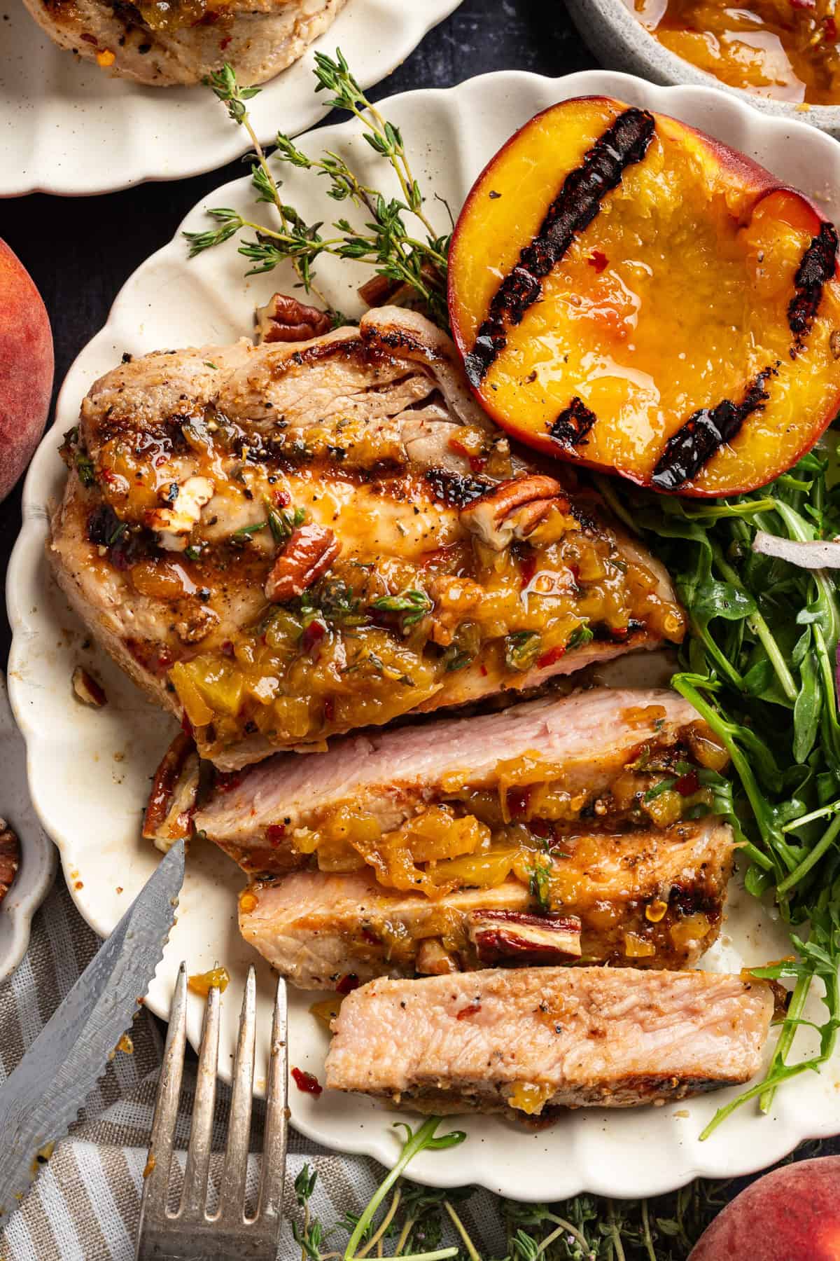Pork Chops with Peaches and Bourbon Glaze Sliced Grilled Pork Chop with grilled peach, arugula, and Peach Bourbon Glaze - on a white plate.