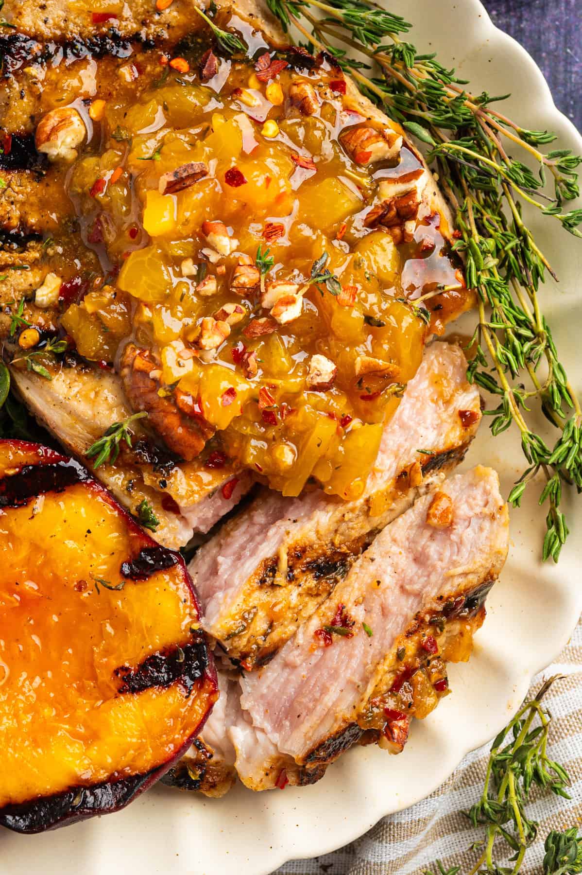 Pork Chops with Peaches and Bourbon Glaze Grilled Pork Chop (sliced) with Grilled Peach and Bourbon Glaze on a white plate.