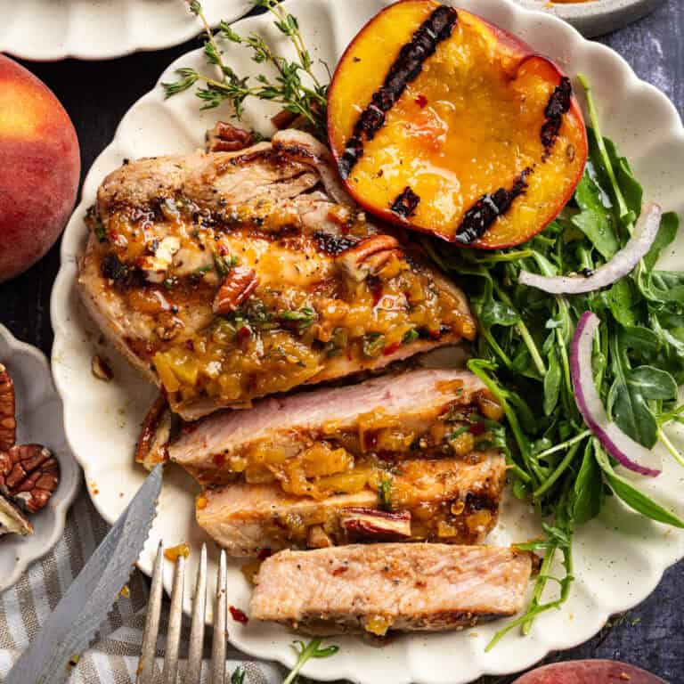 Sliced Grilled Pork Chop with grilled peach, arugula, and Peach Bourbon Glaze - on a white plate.