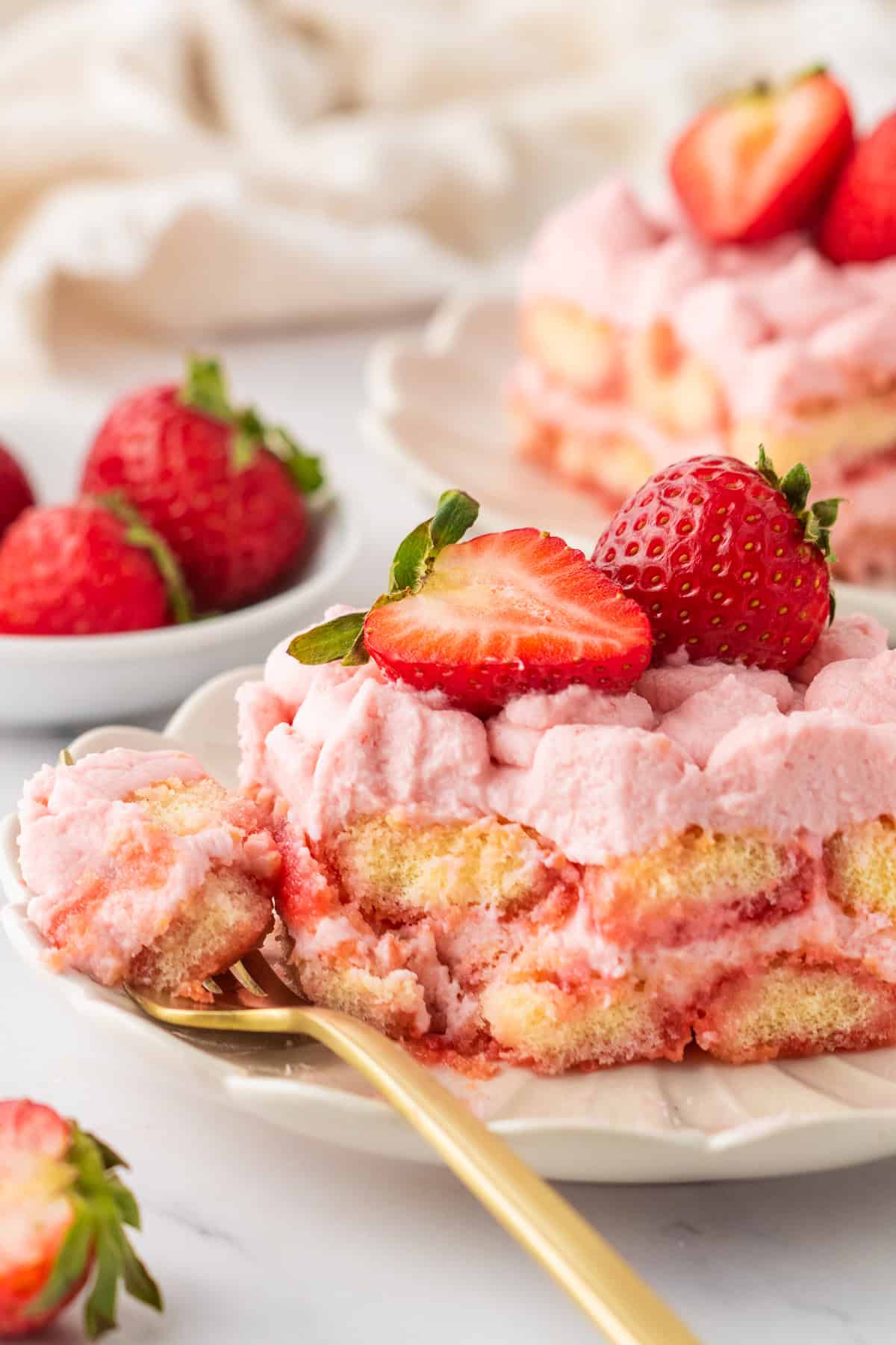 Strawberry Tiramisu A slice of Strawberry Tiramisu (topped with fresh sliced strawberries) on a white plate, with a fork slicing a bite.