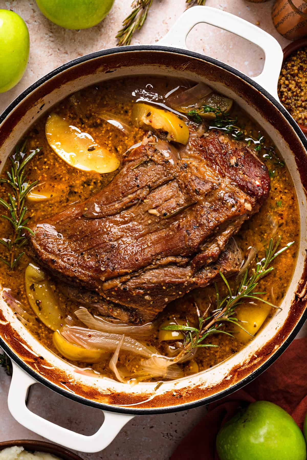 Apple Cider Braised Pork Shoulder with Sliced Apples - in a white Dutch oven.
