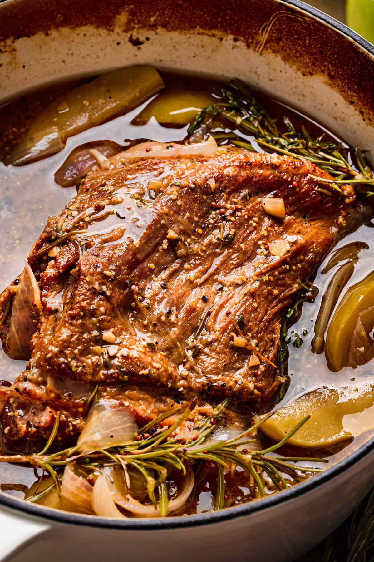 Apple Cider Braised Pork Shoulder with Sliced Apples - in a white Dutch oven.