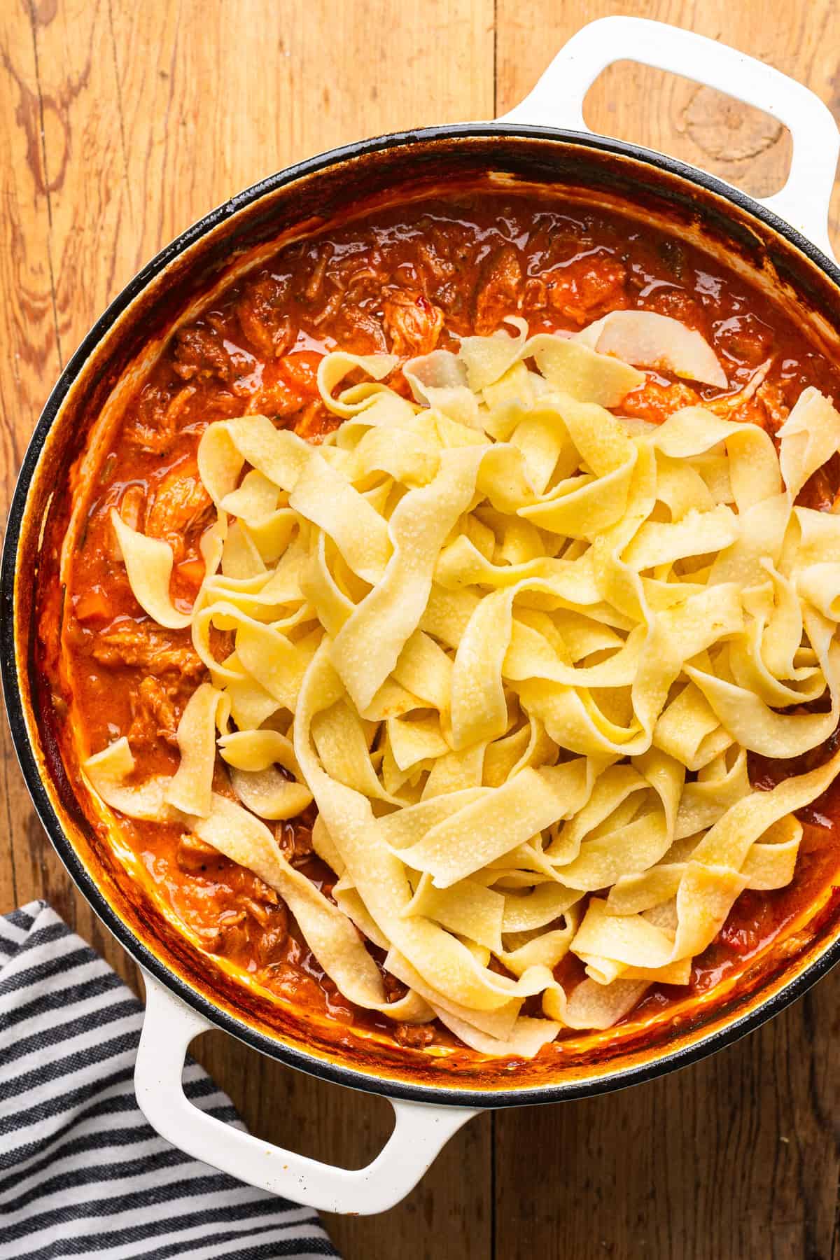 Braised Pork Ragu sauce in a dutch oven, with cooked Pappardelle added on top.