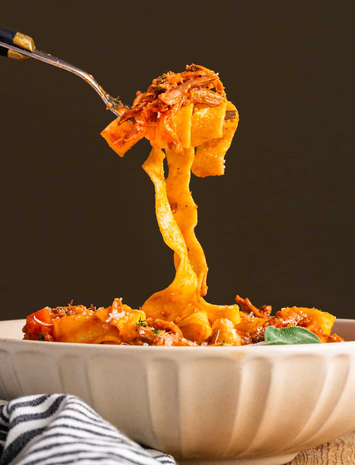 Braised Pork Ragu Pappardelle on a fork extending from a white bowl.
