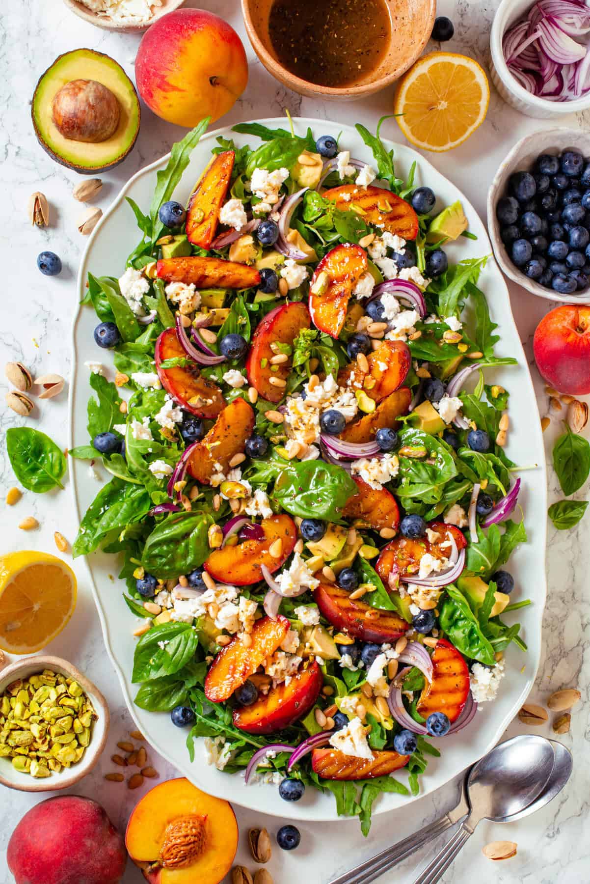 Grilled Peach Salad with Arugula, Blueberries, Feta, Avocado, Pine Nuts, and Pistachios Grilled Peach Salad with Arugula, Blueberries, Feta, Avocado, Pine Nuts, and Pistachios - on a large white platter.