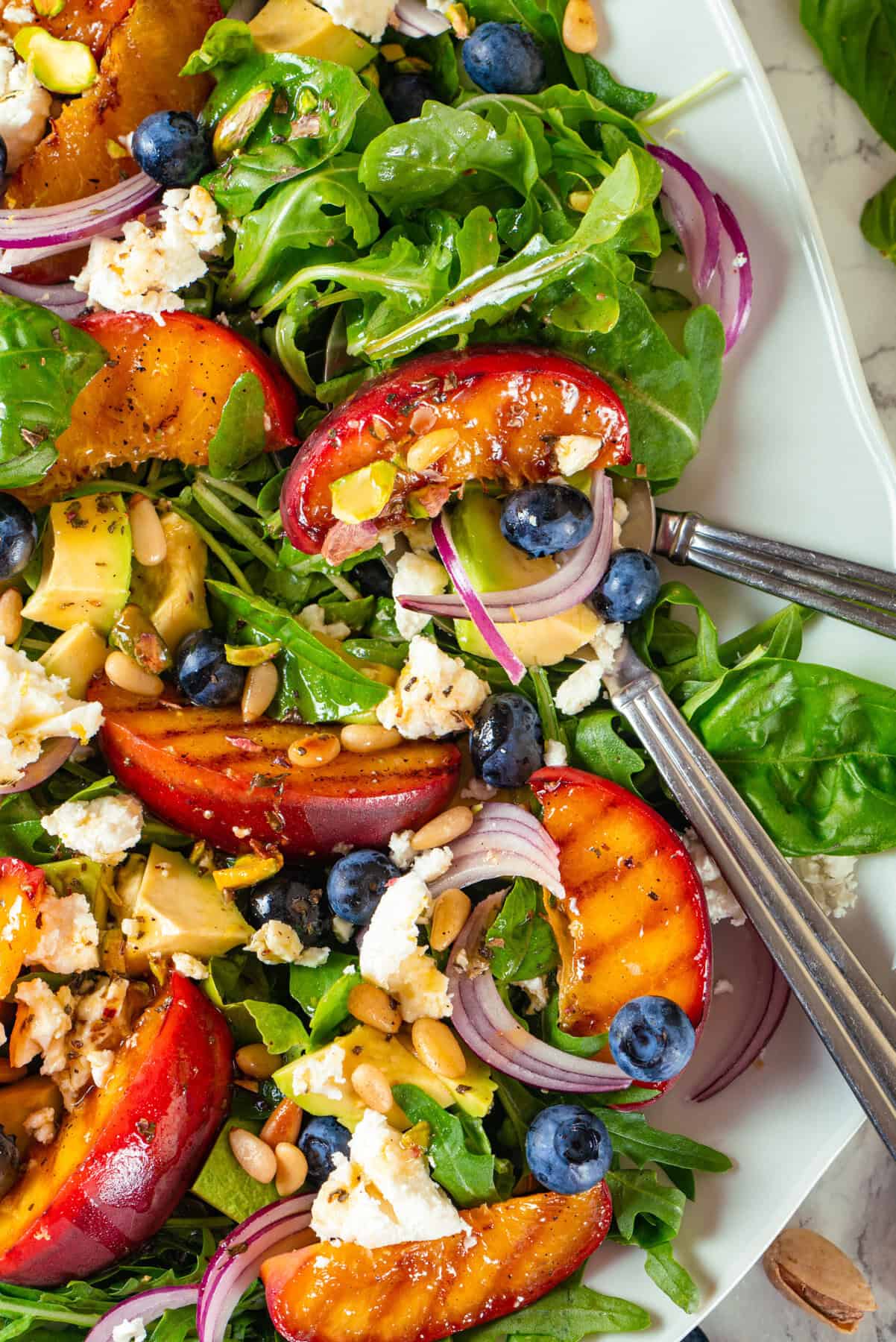 Grilled Peach Salad with Arugula, Blueberries, Feta, Avocado, Pine Nuts, and Pistachios Grilled Peach Salad with Arugula, Blueberries, Feta, Avocado, Pine Nuts, and Pistachios - on a white plate.