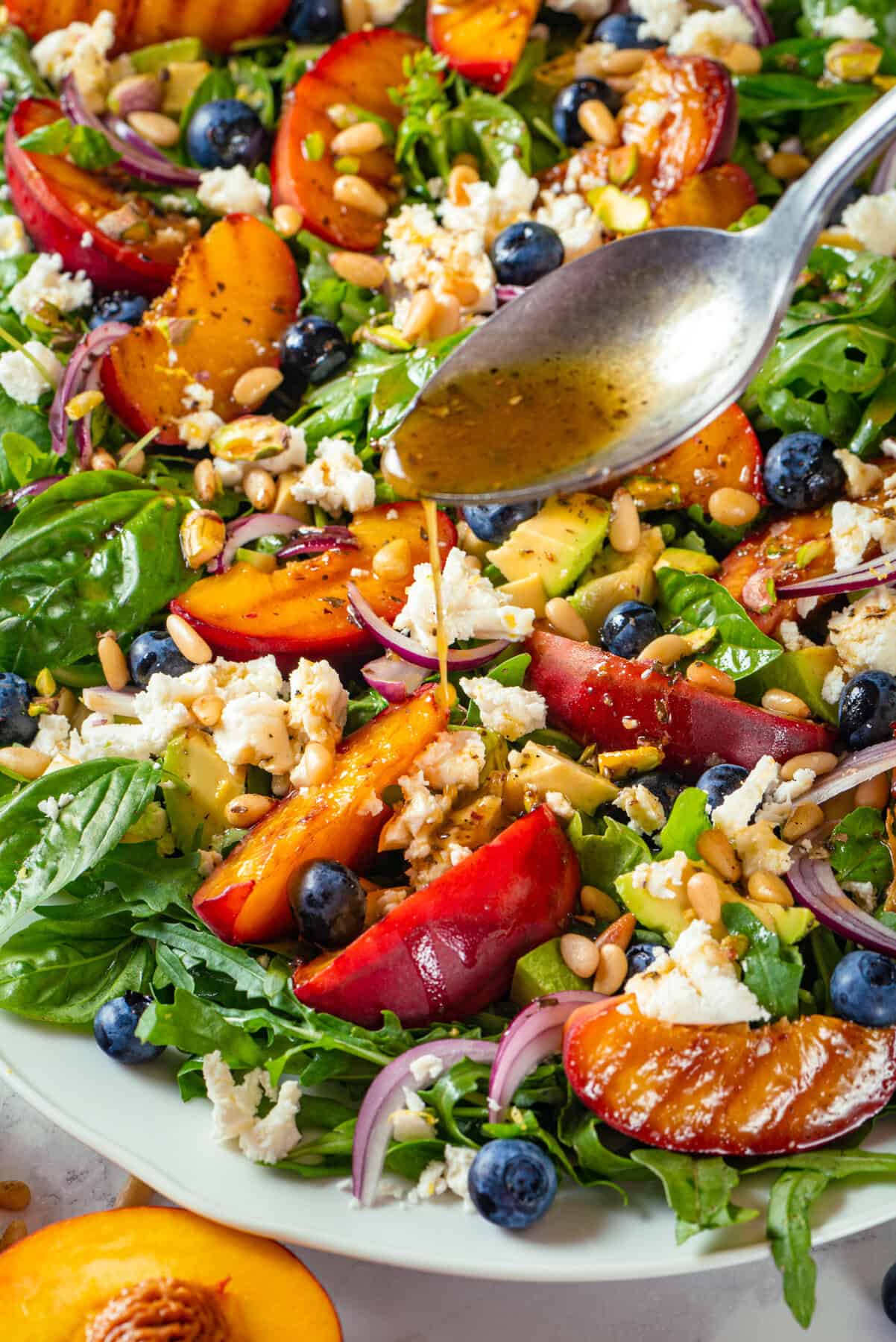 Grilled Peach Salad with Arugula, Blueberries, Feta, Avocado, Pine Nuts, and Pistachios Grilled Peach Salad with Arugula, Blueberries, Feta, Avocado, Pine Nuts, and Pistachios - on a large white platter.