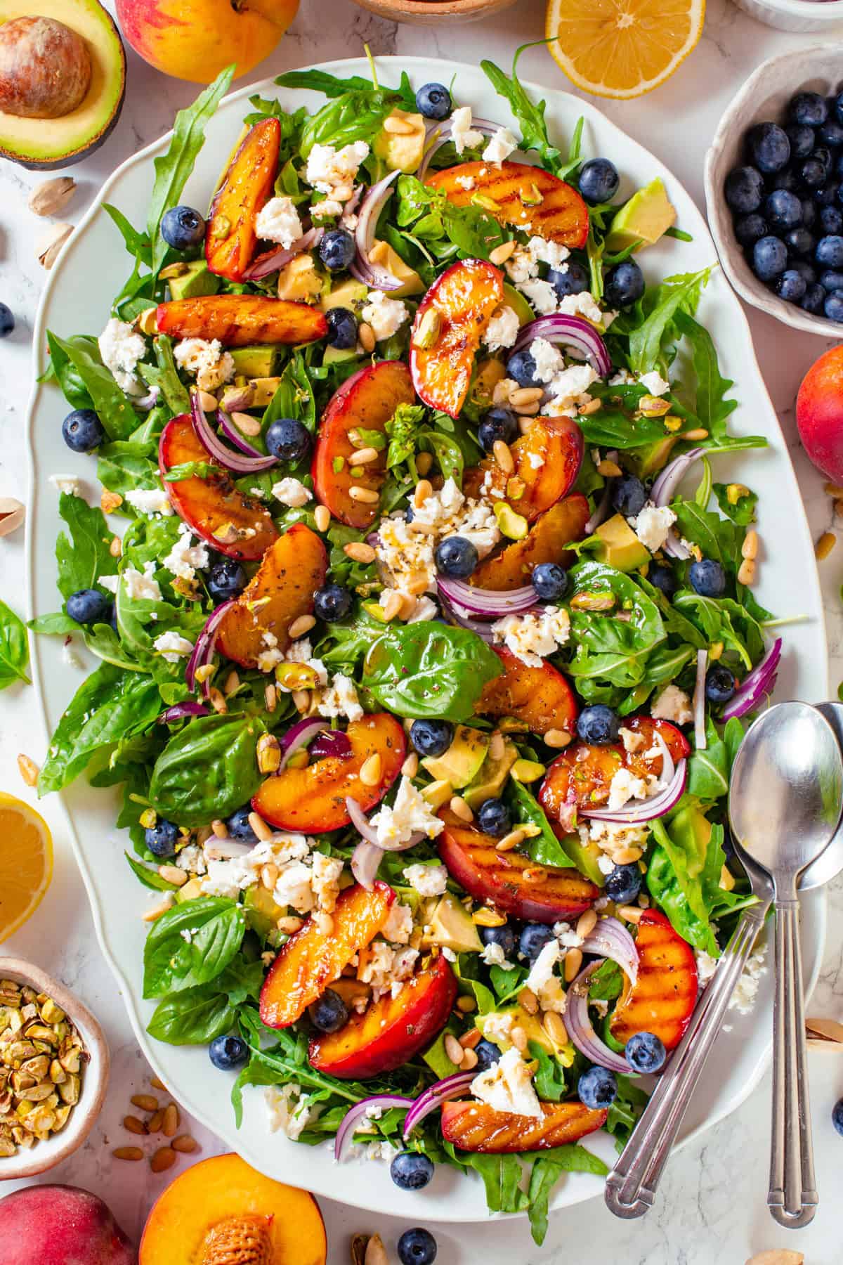 Grilled Peach Salad with Arugula, Blueberries, Feta, Avocado, Pine Nuts, and Pistachios Grilled Peach Salad with Arugula, Blueberries, Feta, Avocado, Pine Nuts, and Pistachios - on a large white platter.