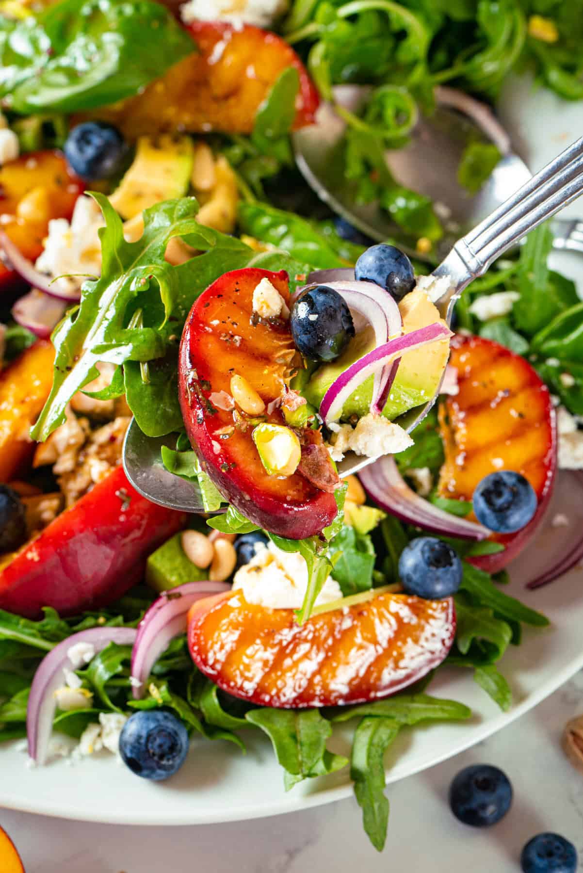 Grilled Peach Salad with Arugula, Blueberries, Feta, Avocado, Pine Nuts, and Pistachios Grilled Peach Salad with Arugula, Blueberries, Feta, Avocado, Pine Nuts, and Pistachios - on a white plate.