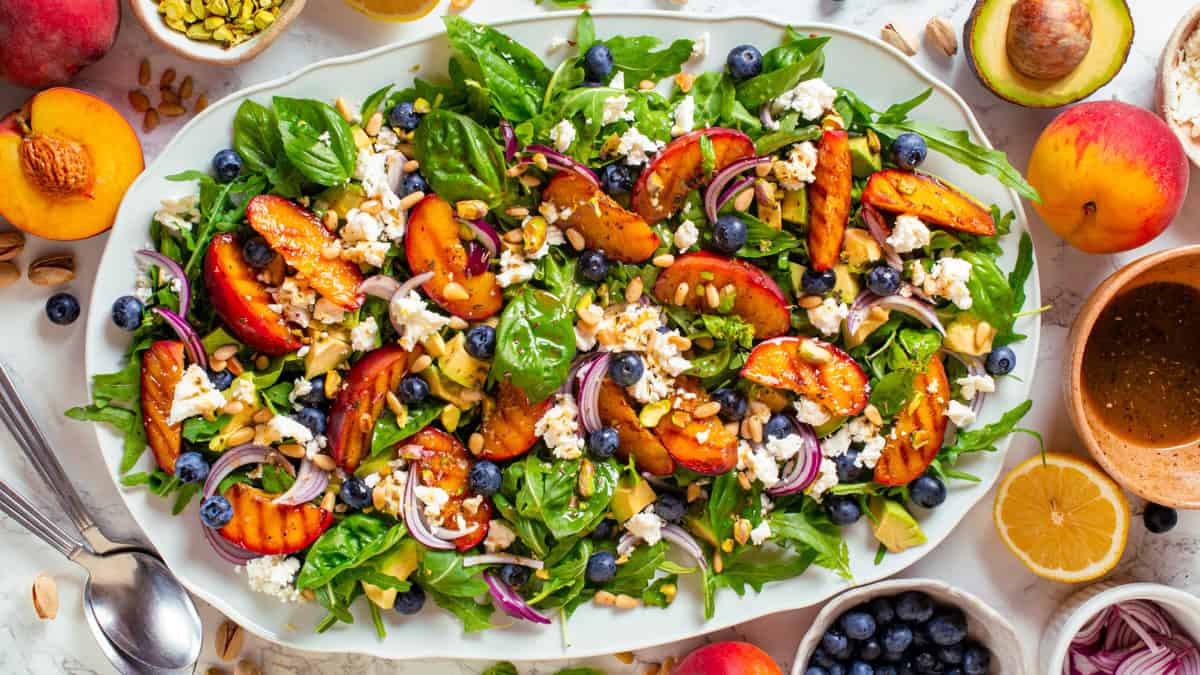 Grilled Peach Salad with Arugula, Blueberries, Feta, Avocado, Pine Nuts, and Pistachios Grilled Peach Salad with Arugula, Blueberries, Feta, Avocado, Pine Nuts, and Pistachios - on a large white platter.