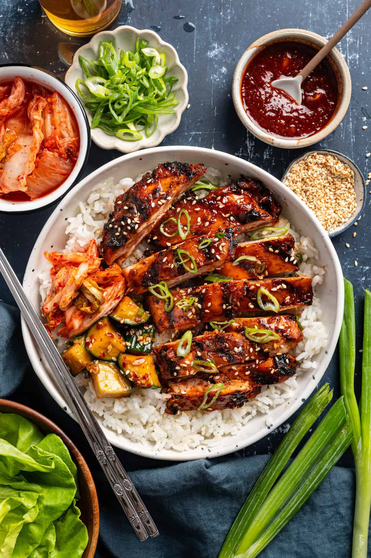 Korean BBQ Chicken with rice, kimchi, and sliced cucumber in a bowl.