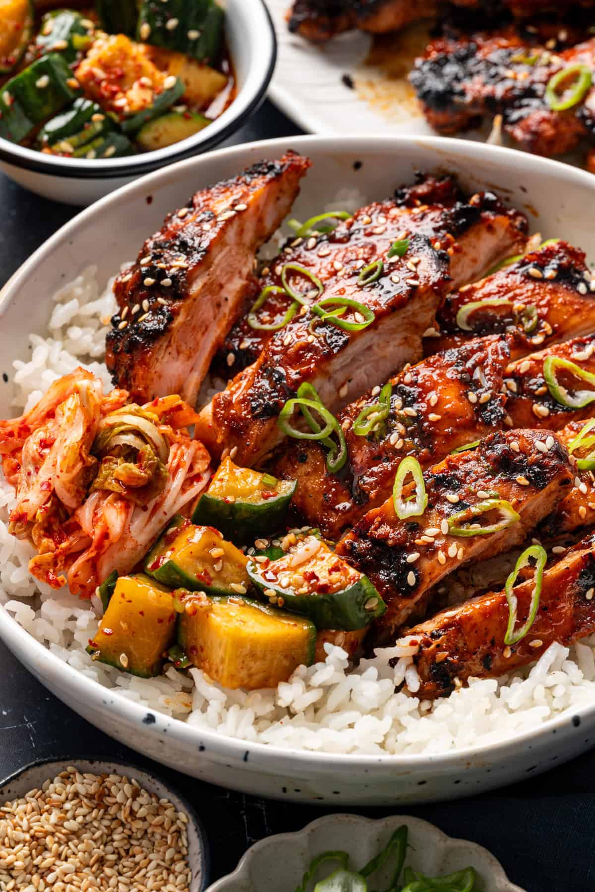 Korean BBQ Chicken with rice, kimchi, and sliced cucumber in a bowl.