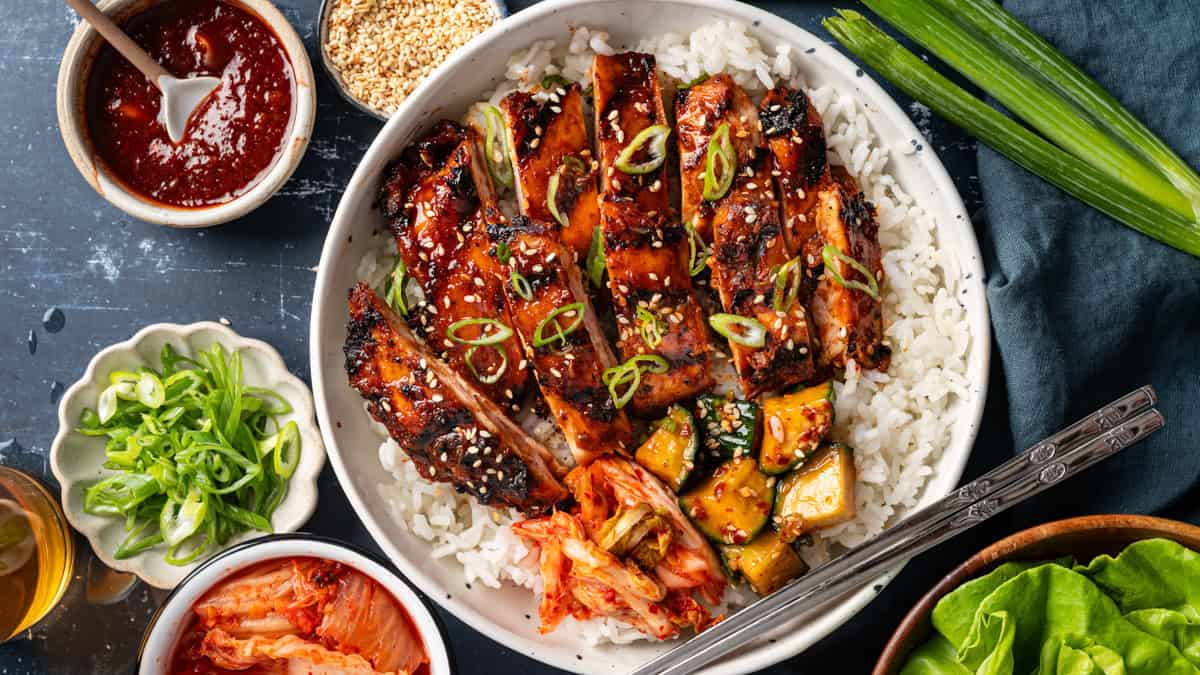 Korean BBQ Chicken with rice, kimchi, and sliced cucumber in a bowl.