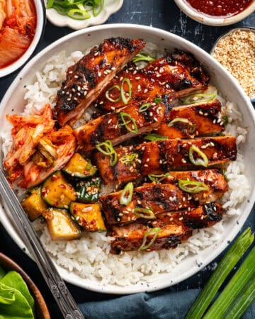 Korean BBQ Chicken with rice, kimchi, and sliced cucumber in a bowl.