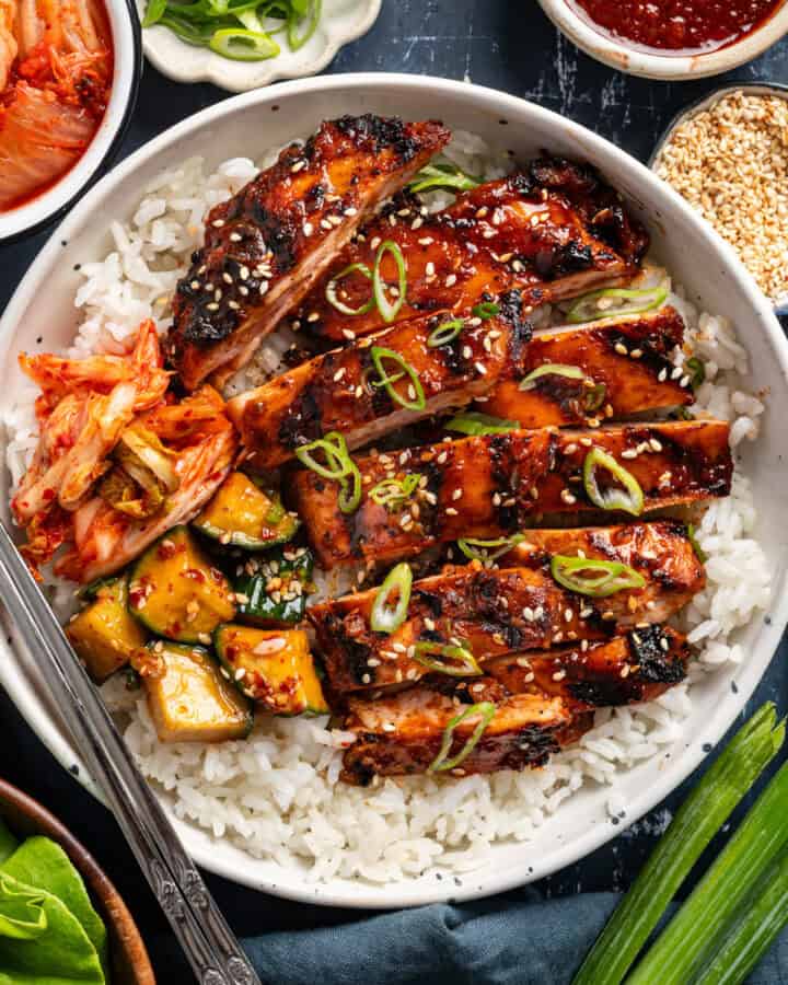Korean BBQ Chicken with rice, kimchi, and sliced cucumber in a bowl.