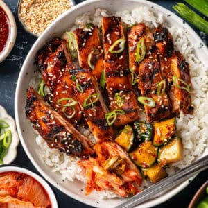 Korean BBQ Chicken with rice, kimchi, and sliced cucumber in a bowl.
