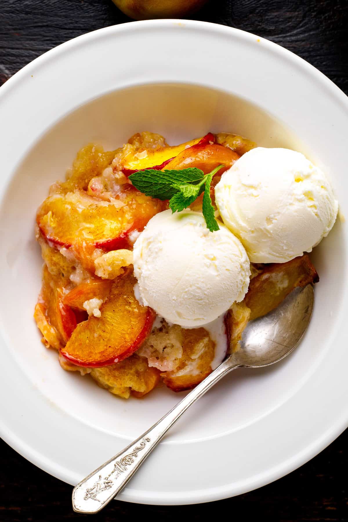Peach Cobbler topped with ice cream in a white bowl.