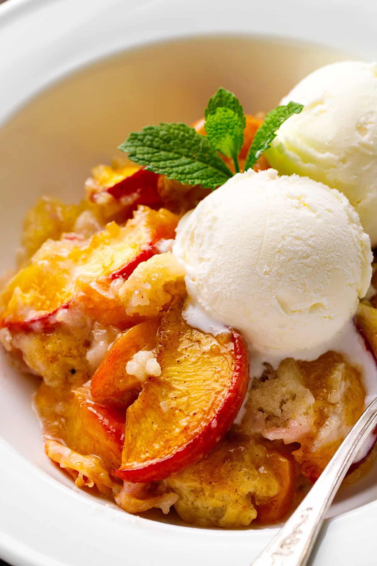 Peach Cobbler topped with ice cream in a white bowl.