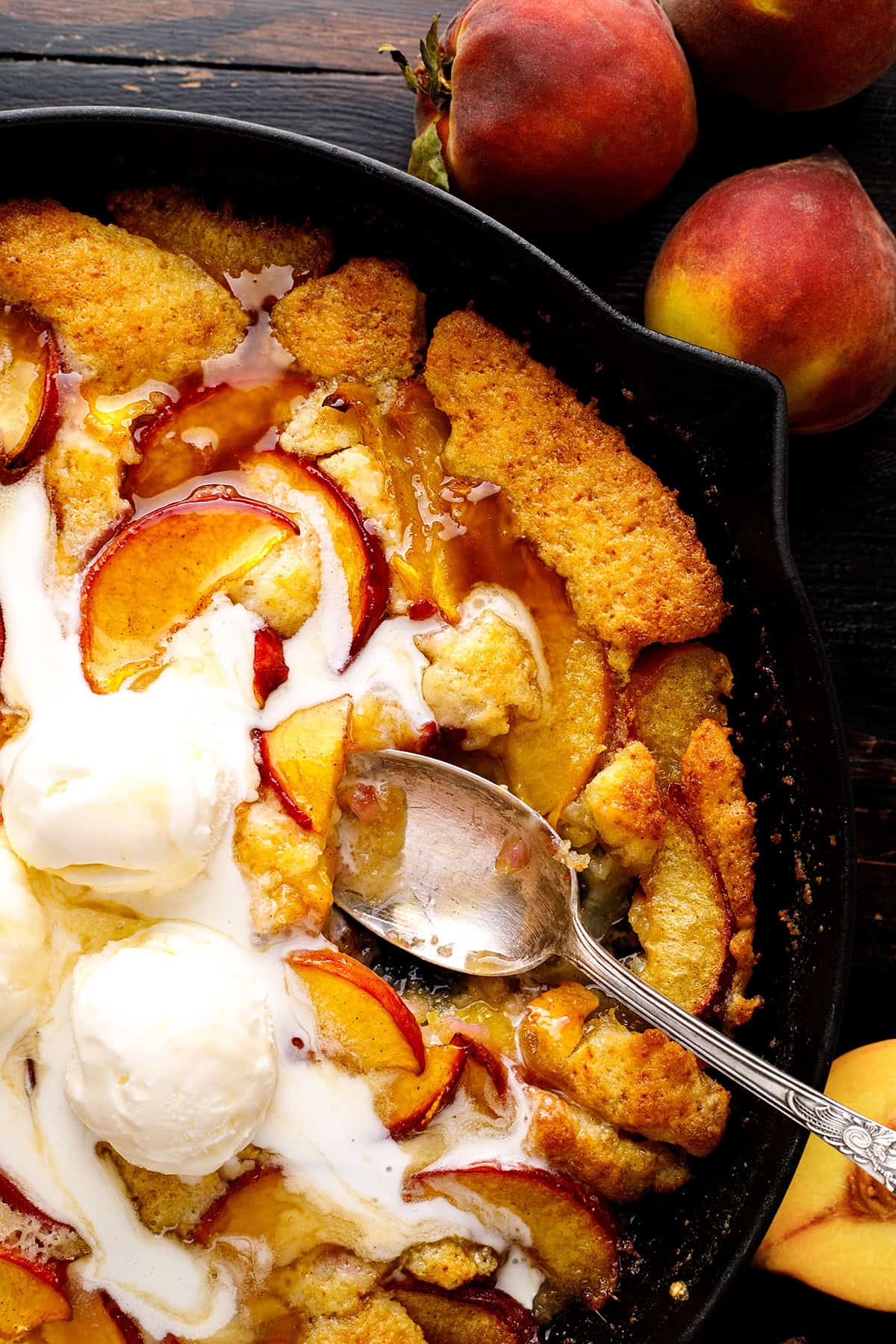 Peach Cobbler topped with ice cream in a black cast iron skillet.