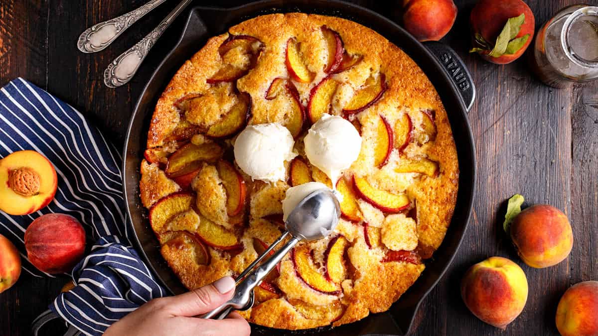 Peach Cobbler topped with ice cream in a black cast iron skillet.