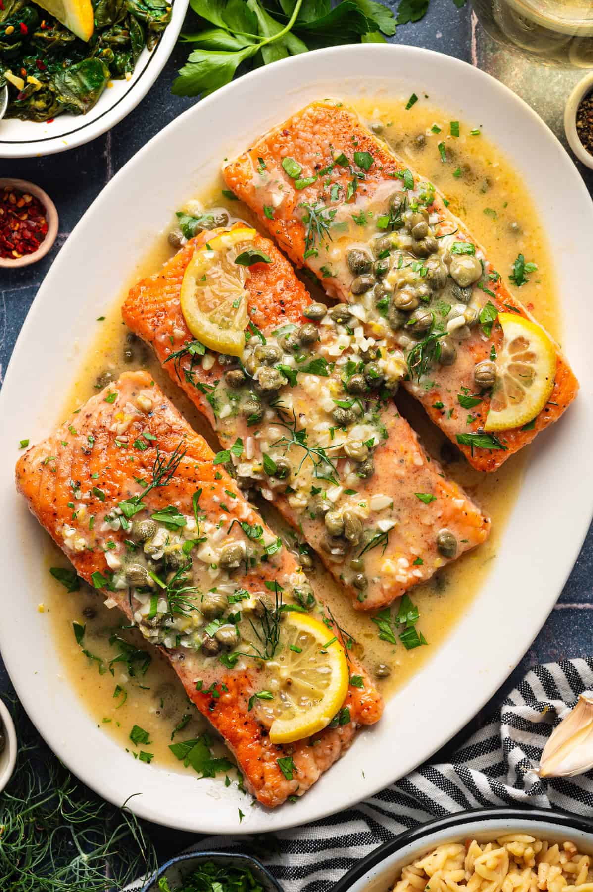 Salmon Piccata Salmon Piccata (3 salmon fillets topped with capers and lemon slices) on a large white platter.