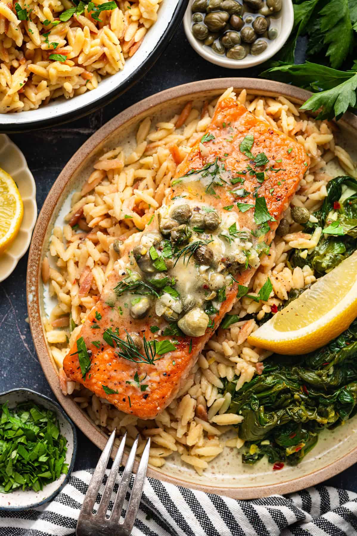 Salmon Piccata with Orzo and Spinach Salmon Piccata - one salmon fillet topped with capers and plated with cooked orzo and spinach on a plate.