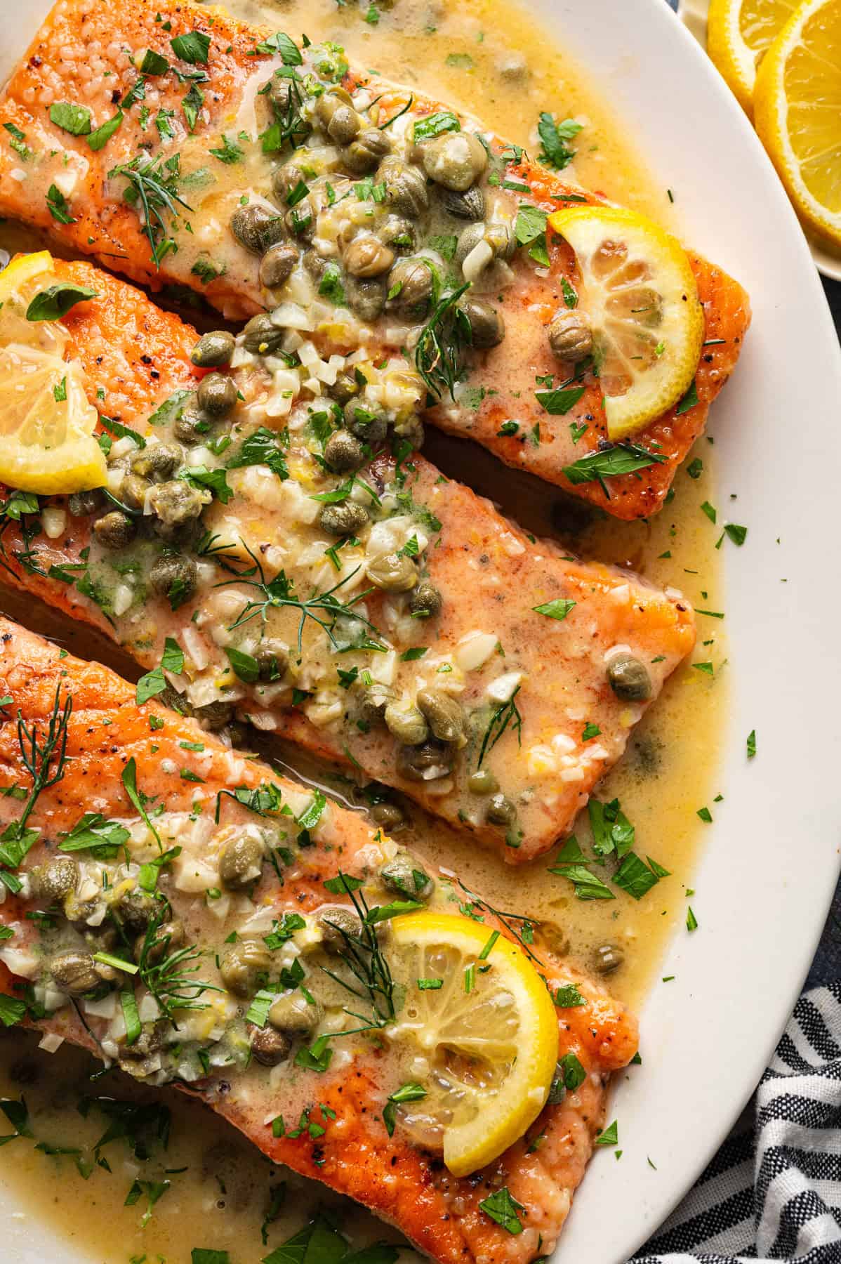 Salmon Piccata Salmon Piccata (3 salmon fillets topped with capers and lemon slices) on a large white platter.