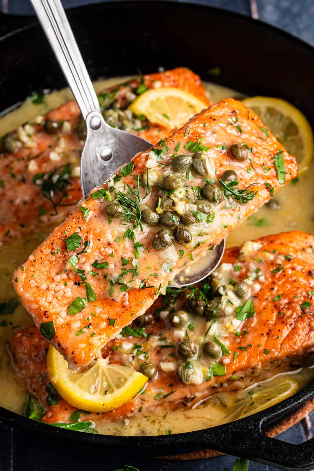 Salmon Piccata Salmon Piccata (3 salmon fillets topped with capers and lemon slices) in a cast iron skillet.