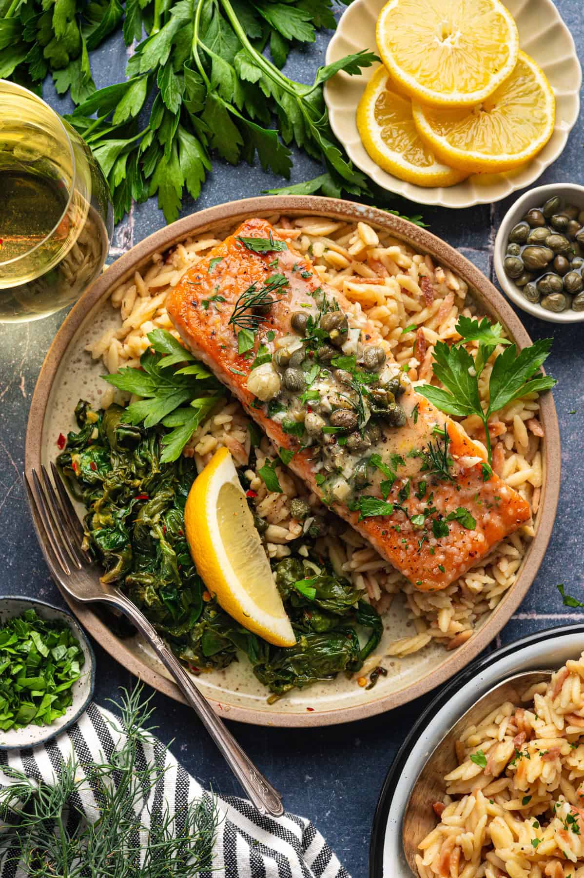 Salmon Piccata with Orzo and Spinach Salmon Piccata - one salmon fillet topped with capers and plated with cooked orzo and spinach on a plate.