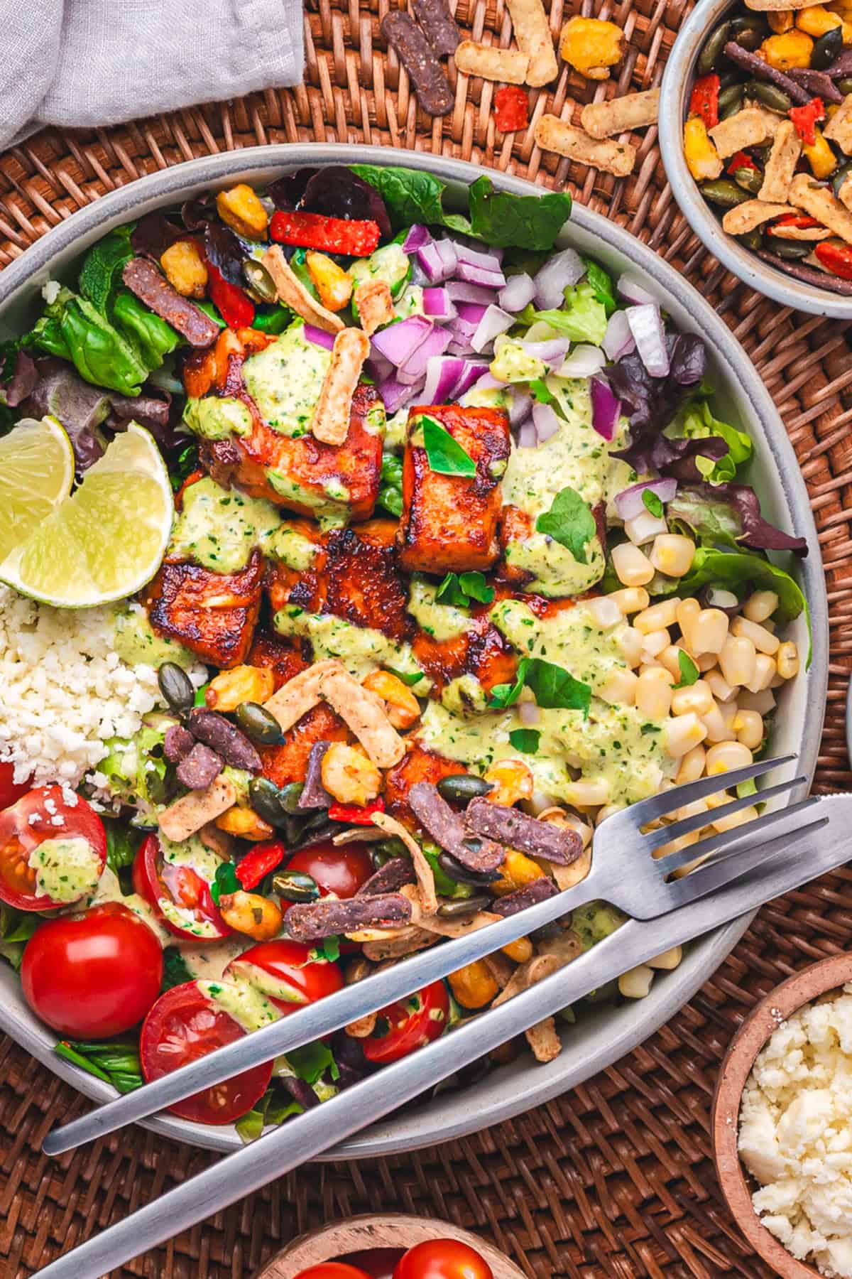 Mexican Salmon Salad Bowl with Roasted Poblano Ranch Salmon taco salad with mixed lettuce, corn, cherry tomatoes, red onion, Cotija cheese, lime wedges, fresh cilantro, and creamy poblano ranch dressing in a bowl.