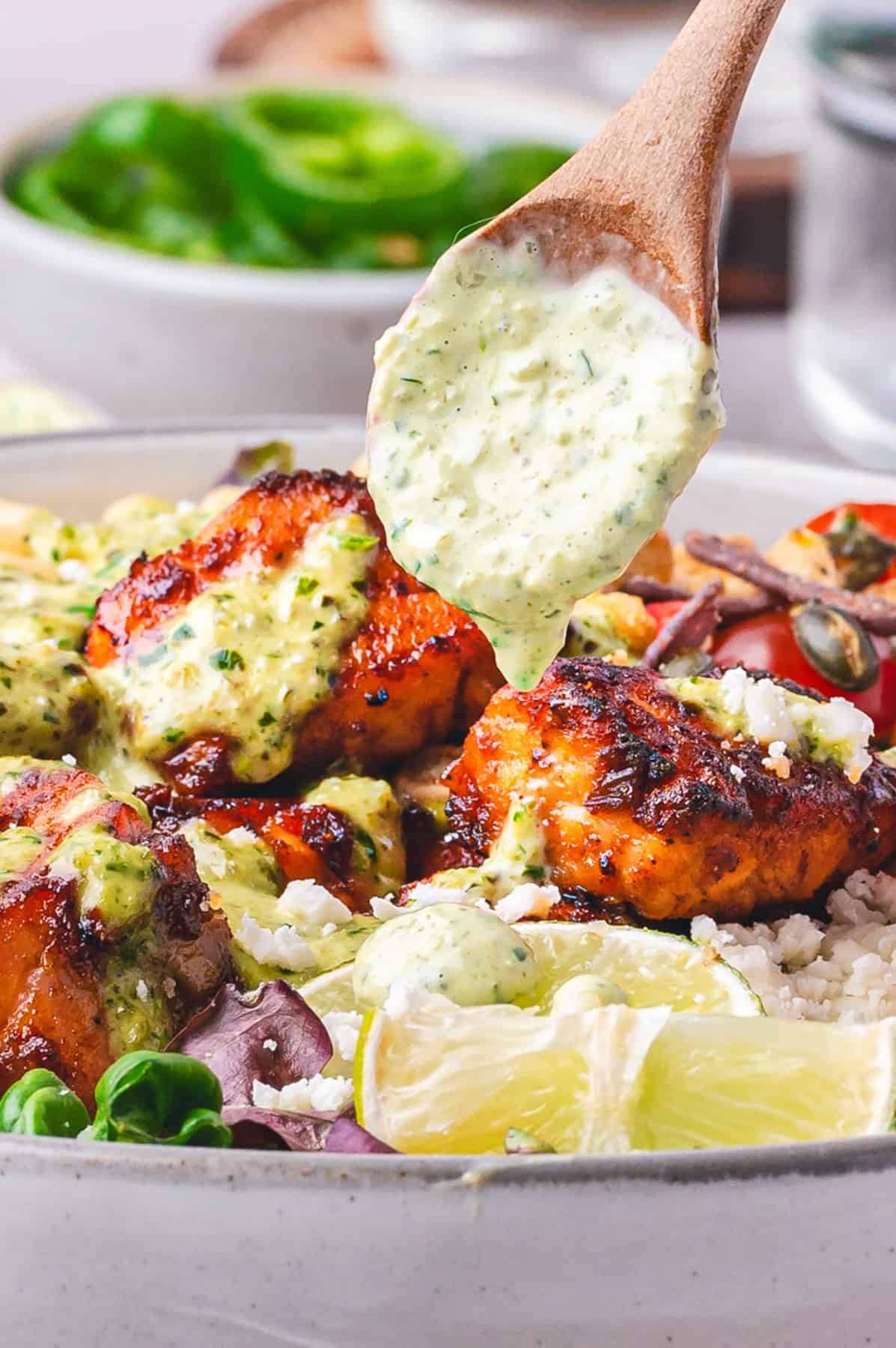 Mexican Salmon Salad Bowl with Roasted Poblano Ranch Salmon taco salad with mixed lettuce, corn, cherry tomatoes, red onion, Cotija cheese, lime wedges, fresh cilantro in a bowl, with creamy poblano ranch dressing drizzled from the spoon.