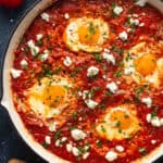 Shakshuka (4 eggs poached in a spiced tomato, pepper, and onion sauce) in a white pan.