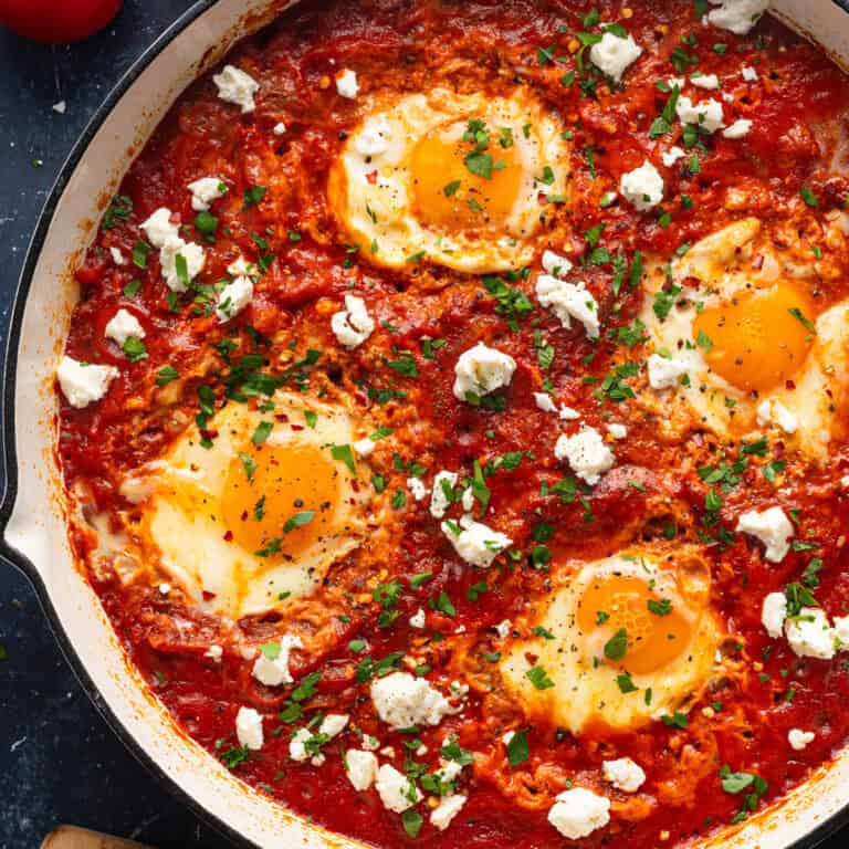 Shakshuka (4 eggs poached in a spiced tomato, pepper, and onion sauce) in a white pan.