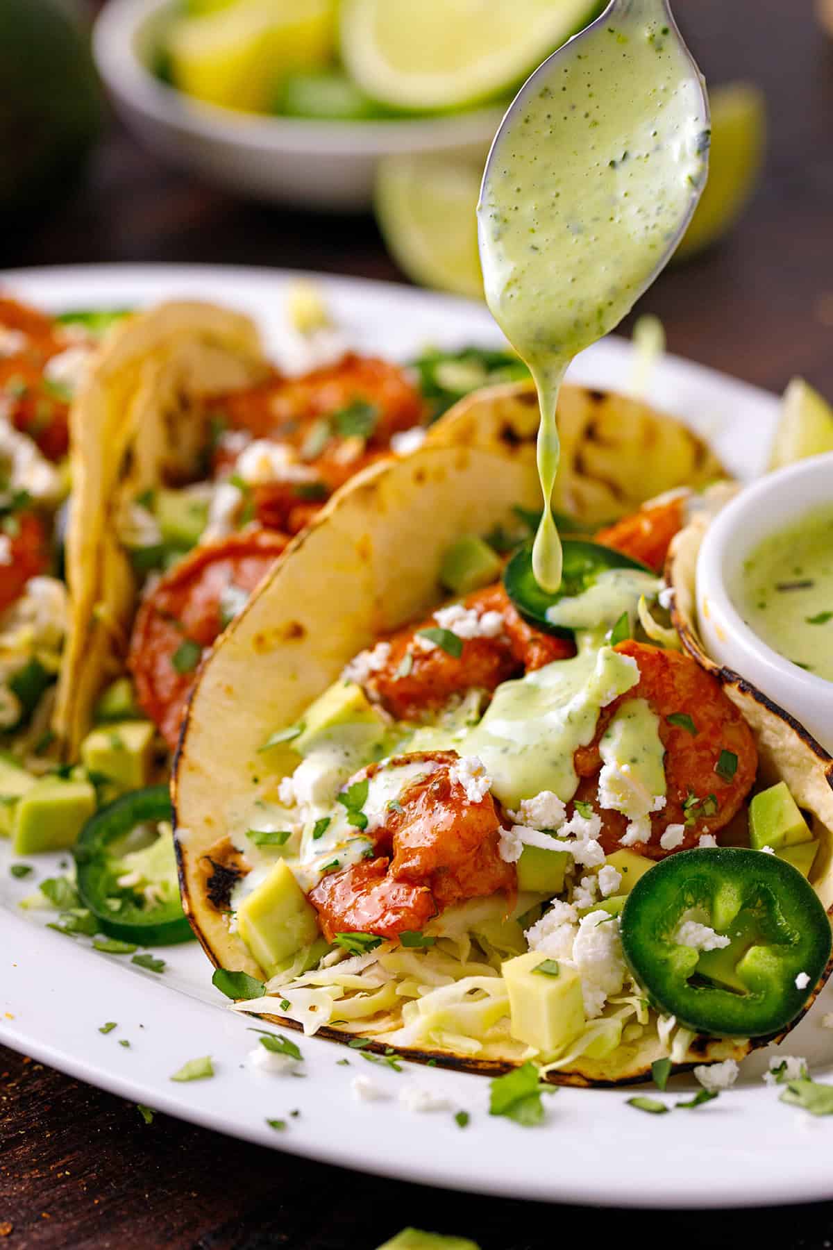 Shrimp Tacos Shrimp Tacos with light green cilantro sauce being poured over the taco.