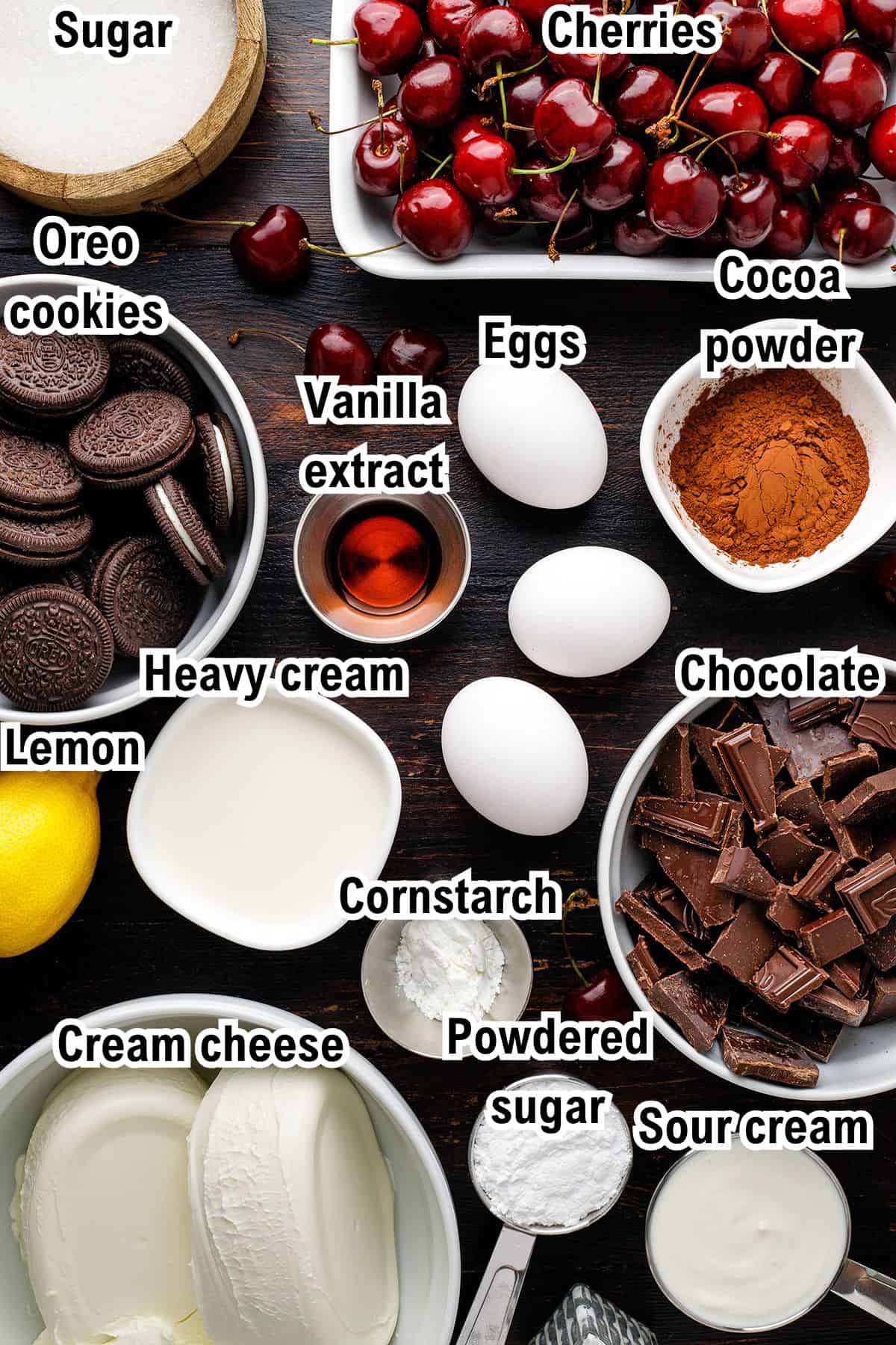 The Ingredients for Black Forest Cheesecake A flat lay of labeled ingredients for Black Forest Cheesecake including sugar, cherries, Oreo cookies, vanilla extract, eggs, cocoa powder, heavy cream, chocolate, lemon, cornstarch, powdered sugar, cream cheese, and sour cream.