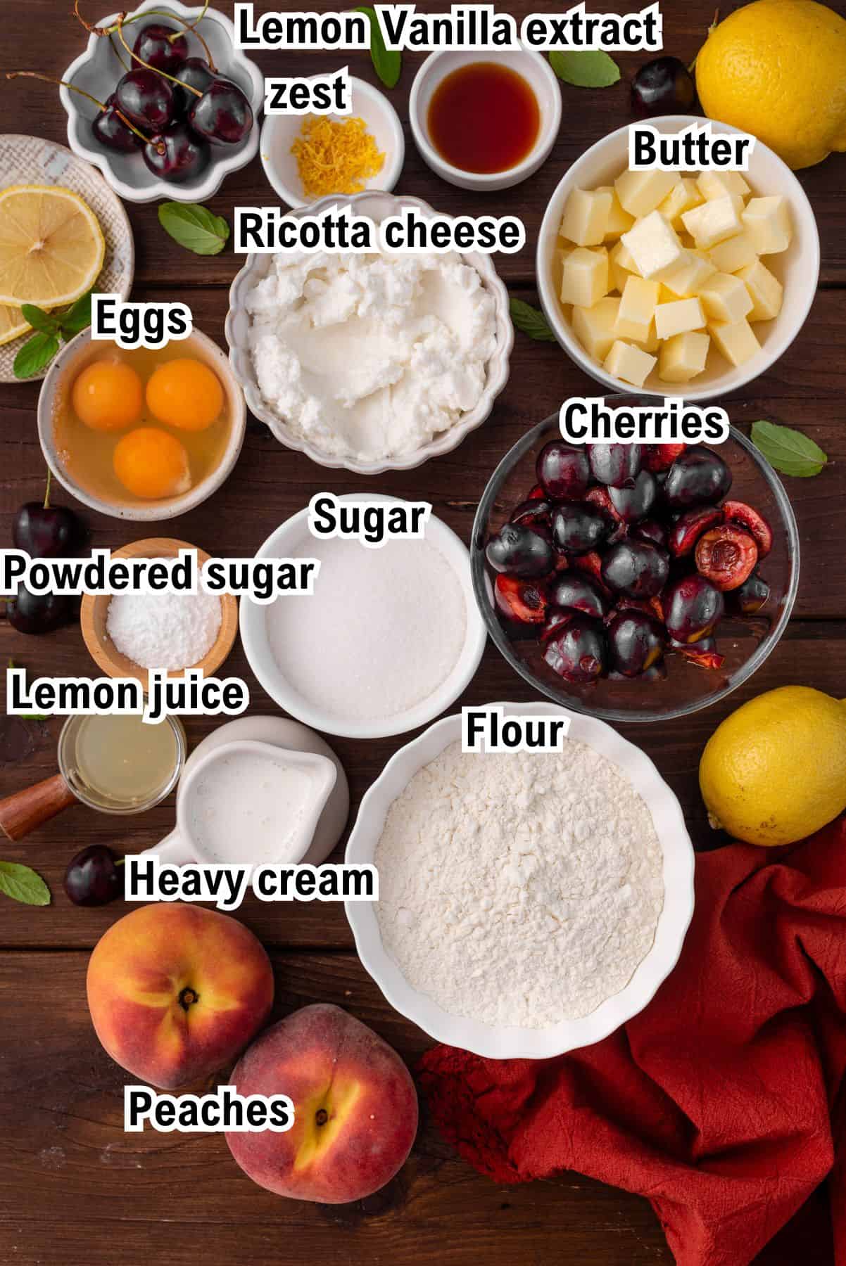 The Ingredients for Cherry Peach Ricotta Cake This photo shows the ingredients for Cherry Peach Ricotta Cake including eggs, ricotta, cherries, peaches, heavy cream, lemon, powdered sugar, regular sugar, flour, butter, vanilla extract, and lemon zest on a wooden table.