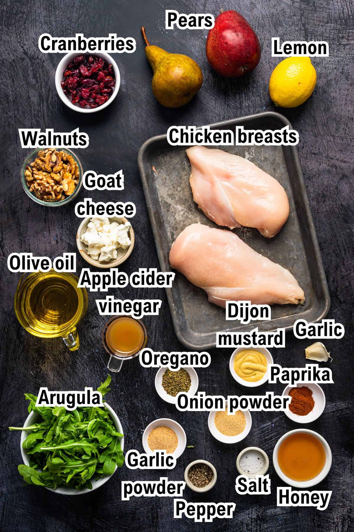 The Ingredients for Chicken Arugula Salad This photo shows the ingredients for Chicken Arugula Salad: Chicken breasts on a tray surrounded by labeled ingredients: cranberries, pears, lemon, walnuts, goat cheese, olive oil, apple cider vinegar, Dijon mustard, garlic, paprika, oregano, onion powder, garlic powder, pepper, salt, honey, arugula.