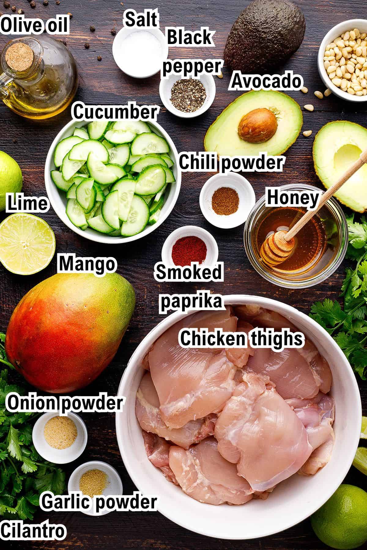 The Ingredients for Grilled Cilantro Lime Chicken Thighs This photo shows the ingredients for a cilantro-lime grilled chicken recipe: chicken thighs, sliced cucumber, avocado, mango, olive oil, honey, lime, and spices, including salt, black pepper, chili powder, smoked paprika, onion and garlic powder, and cilantro.