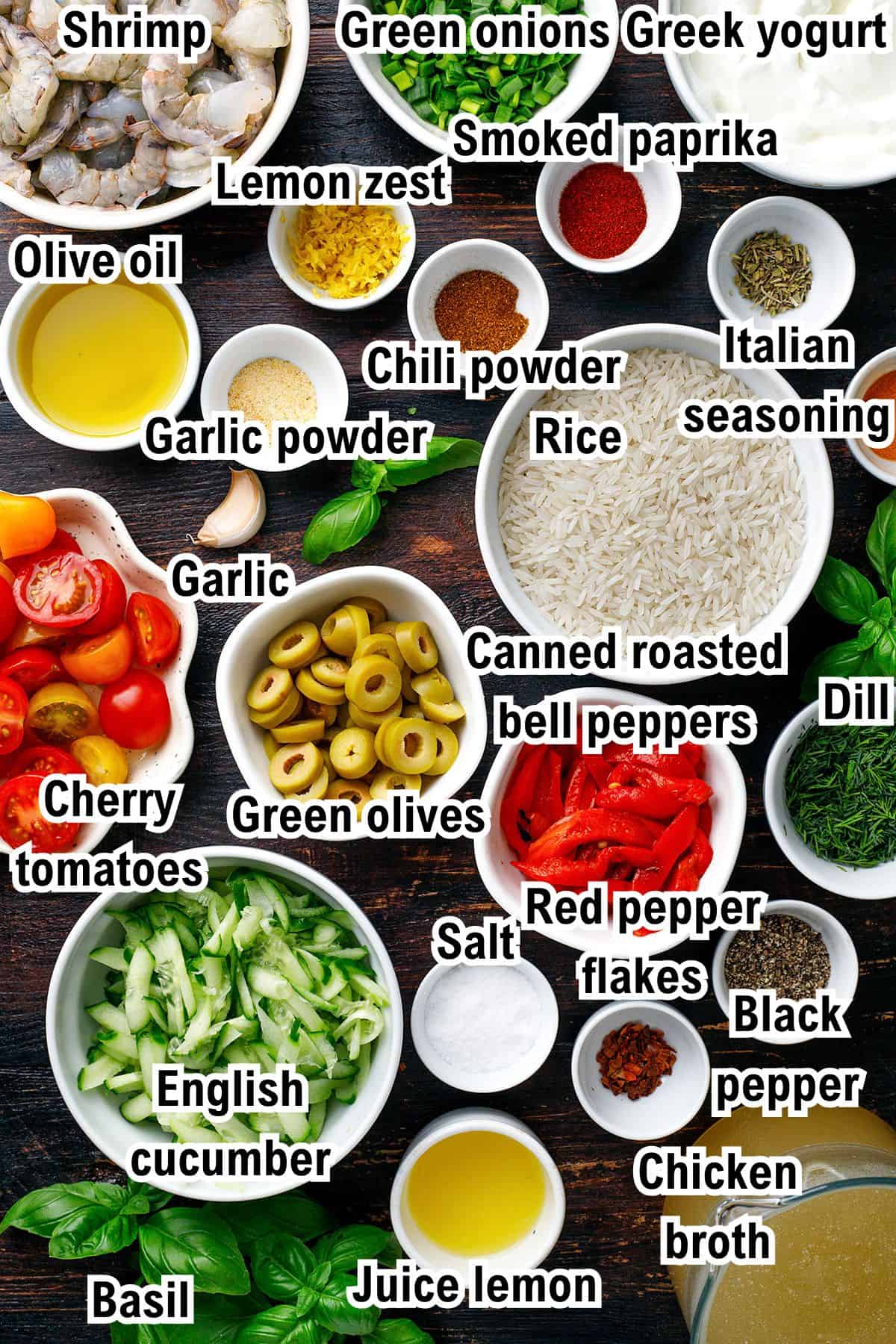 A variety of ingredients for Greek shrimp and lemon rice in bowls and plates on a black surface, labeled: shrimp, green onions, Greek yogurt, smoked paprika, olive oil, lemon zest, garlic powder, chili powder, Italian seasoning, rice, garlic, canned roasted bell peppers, cherry tomatoes, green olives, English cucumber, salt, red pepper flakes, black pepper, chicken broth, basil, juice lemon, and dill.