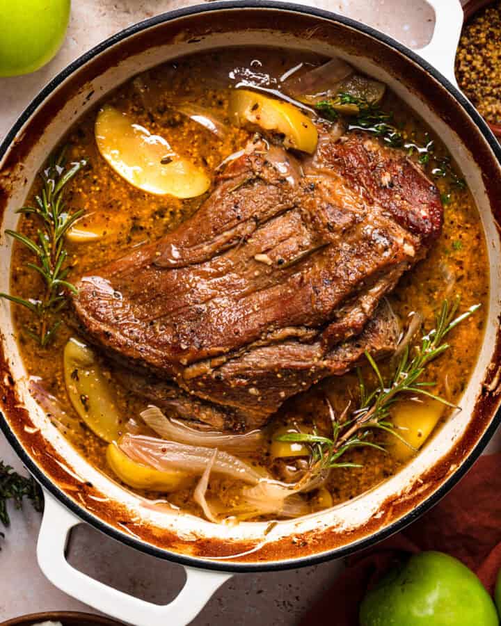 Apple Cider Braised Pork Shoulder with Sliced Apples - in a white Dutch oven.