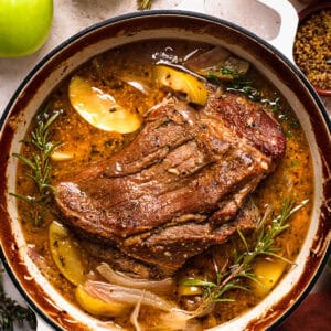 Apple Cider Braised Pork Shoulder with Sliced Apples - in a white Dutch oven.