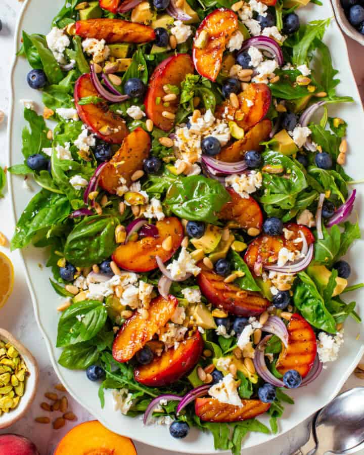 Grilled Peach Salad with Arugula, Blueberries, Feta, Avocado, Pine Nuts, and Pistachios - on a large white platter.