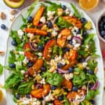 Grilled Peach Salad with Arugula, Blueberries, Feta, Avocado, Pine Nuts, and Pistachios - on a large white platter.