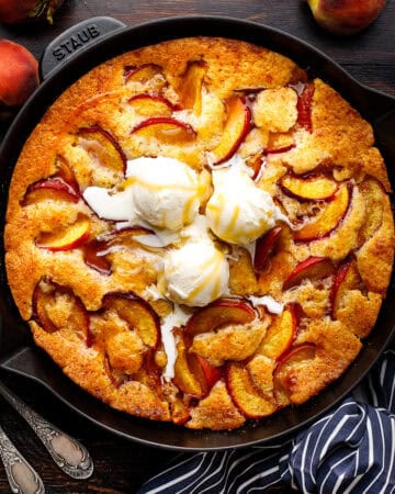 Peach Cobbler drizzled with Bourbon Maple Glaze and topped with ice cream in a black cast iron skillet.