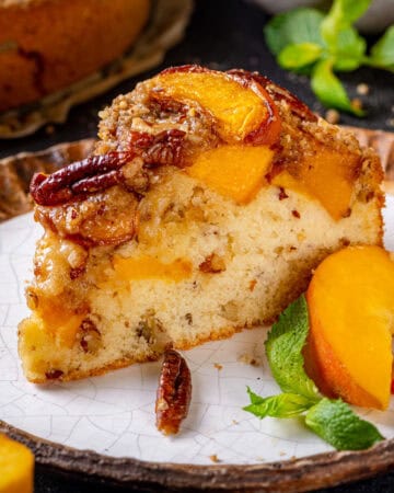 A slice of Peach Coffee Cake topped with Pecan Streusel and Peach Slices - on a plate.