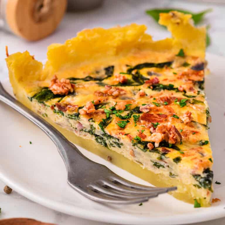 A slice of Potato Crust Quiche with Bacon and Spinach Filling on a plate.